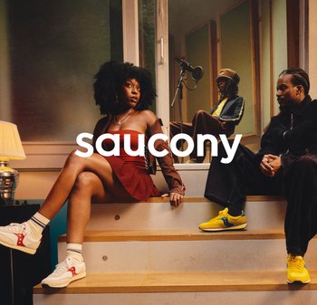 Baskets Saucony : blanches avec des accents rouges et semelle grise ; baskets jaunes avec des accents bleus. L'arrière-plan présente un éclairage doux et des escaliers en bois.