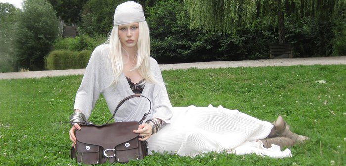 Brown leather handbag with silver hardware, large front pocket, and double top handle. Model wears grey top and white textured skirt.
