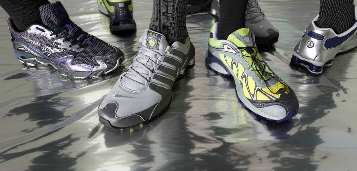 Štiri para športnih copat: črno in srebrno mrežasto, sivo usnje, sivo in neonsko rumeno mrežasto ter sijoče srebrno z modrimi poudarki. Teksturirane površine.