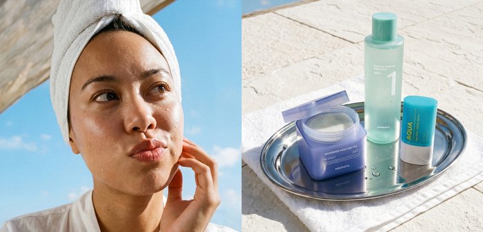 Femme avec une serviette sur la tête touchant sa joue à côté d'un plateau contenant trois produits de soin de la peau sur un tissu blanc au soleil.