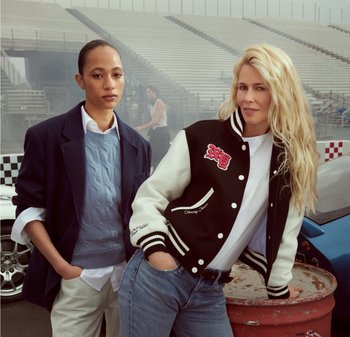 Deux femmes se tiennent ensemble, l'une dans un pull en mailles bleu et un pantalon beige, l'autre dans une veste de style universitaire noir et blanc avec des accents rouges.