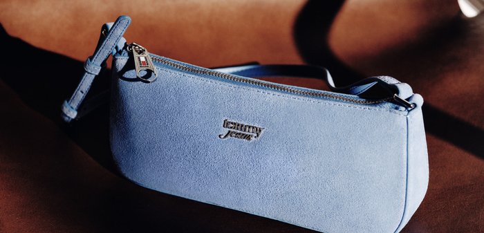 Lichtblauw suède polstasje van Tommy Jeans met ritssluiting en klein metalen logo op een bruin oppervlak.