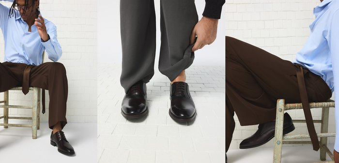 Man draagt zwarte nette schoenen en hijst zijn donkergrijze broekspijp omhoog, waarbij zijn enkel zichtbaar wordt tegen een achtergrond van witte tegelvloer.