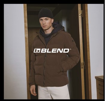 Bruine donsjas met rits aan de voorkant, capuchon en zijzakken, gedragen over een zwarte trui. Aangevuld met een zwarte muts.