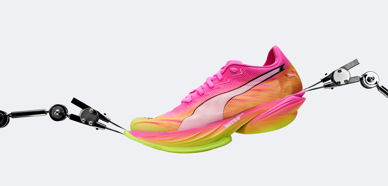 Φούξια και κίτρινο παπούτσι για τρέξιμο που τεντώνεται από δύο ρομποτικά χέρια πάνω σε απλό φωτεινό φόντο.