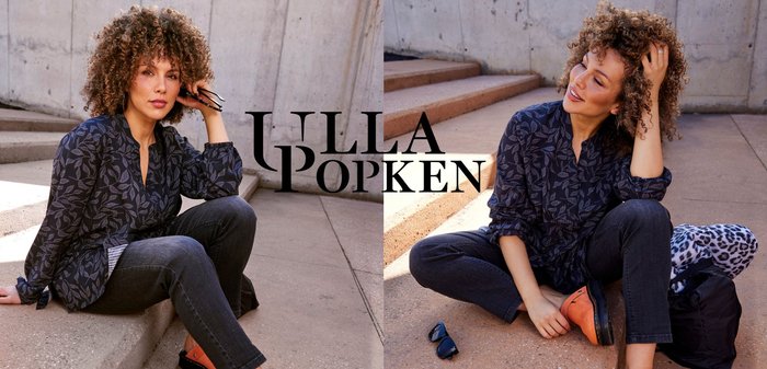 Marineblouse met bladenpatroon, donkere jeans en oranje klompen. Model zit op betonnen treden, met zonnebril en een gedrukt tas in de buurt.