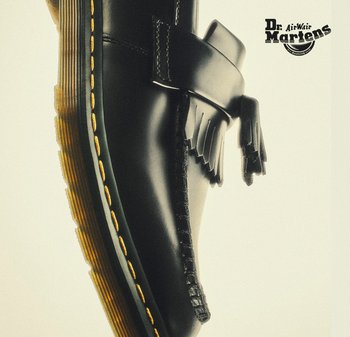 Zwarte leren schoen met een decoratieve band, voorzien van franjes. Dikke rubberen zool met gele stiksels en een ronde neus.