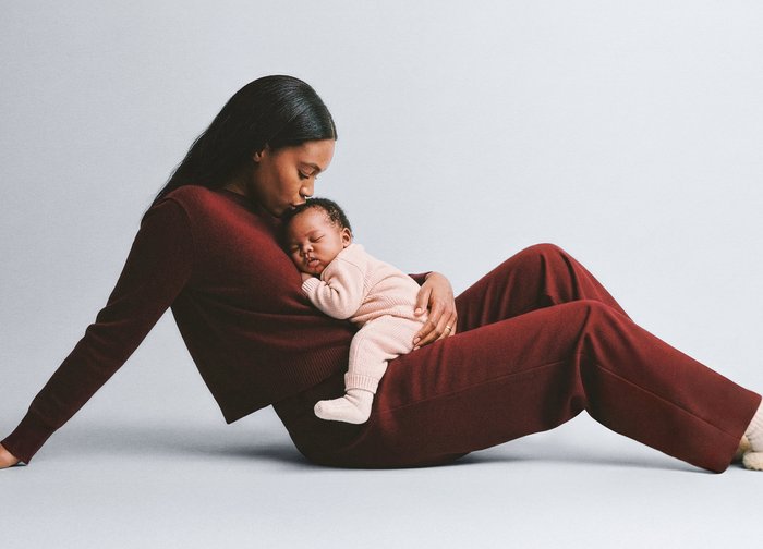 Pull en maille bordeaux et pantalon portés par une femme, assise avec un nourrisson endormi vêtu d'une tenue en maille rose clair, reposant contre sa poitrine.