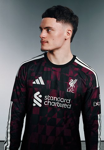 Junger Mann mit kurzen dunklen Haaren, der ein Liverpool FC Fußballtrikot trägt und seitlich vor einem schlichten Hintergrund schaut.