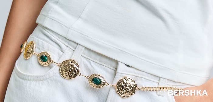 Curea lanț din aur cu medalioane mari texturate și pietre ovale verzi, purtată în jurul taliei blugilor albi.