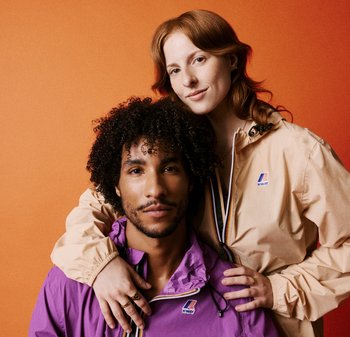 Giacche viola e beige con logo K-Way; colori a contrasto e tessuto leggero. I modelli hanno capelli ricci e lisci; sfondo neutro.