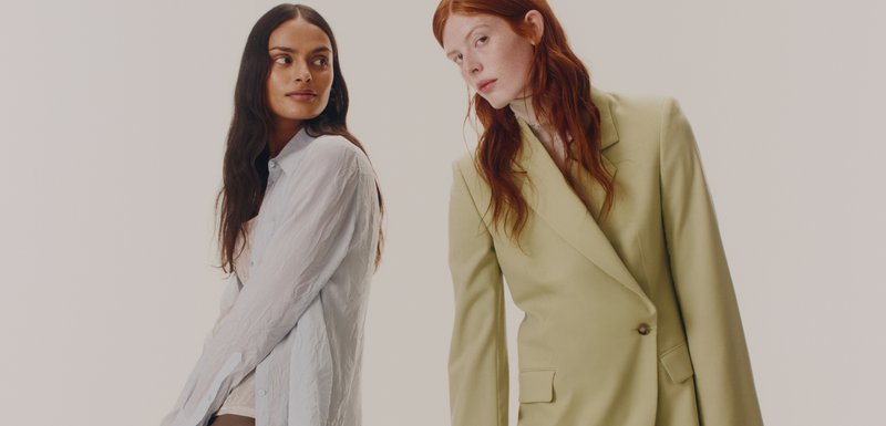 Δύο μοντέλα παρουσίαζονται: το ένα φοράει ένα ανοιχτό μπλε, τσαλακωμένο πουκάμισο και το άλλο ένα προσαρμοσμένο, διπλό ραμμένο, λαχανί σακάκι.