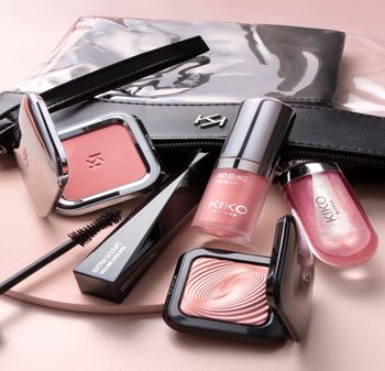 Cosmetic products on a pastel background: a pink trio blush, a glossy lip oil, a black mascara, and a textured highlighter in sleek packaging.