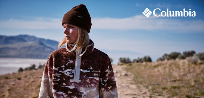 Braun-weiß gemusterter Fleece-Pullover mit hohem Kragen und Knopfleiste. Getragen mit einer braunen Mütze, kombiniert mit hellbraunen Hosen.