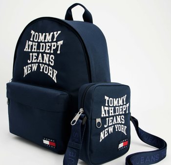 Granatowy plecak z zaokrąglonym dnem, przednią kieszenią i regulowanymi szelkami; z białym napisem: "TOMMY ATH.DEP.T JEANS NEW YORK." Obejmuje małą torebkę.