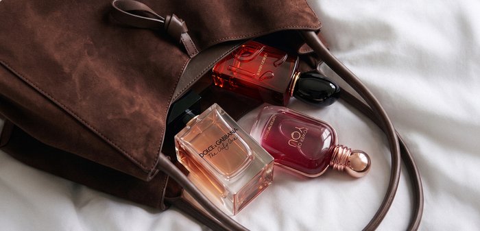 Bruine leren handtas op witte stof met drie parfumflesjes gedeeltelijk erin, inclusief Dolce & Gabbana The Only One.
