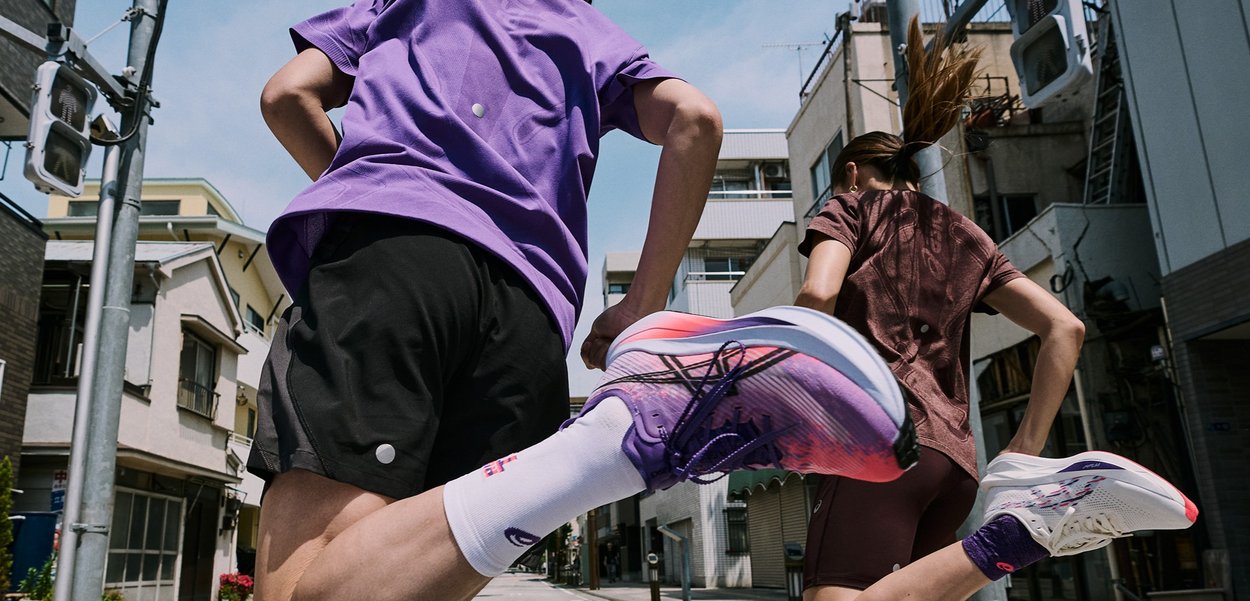 Baskets de course avec un design dégradé rose-violet, tige en mesh léger, semelle rembourrée, portées avec un short noir et des chaussettes blanches.