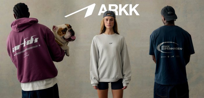 Mulher de frente usando sweatshirt cinzento e boné preto virado para trás; homem de costas com camisa azul-marinho e boné escuro, logótipo da ARKK Copenhagen no centro.