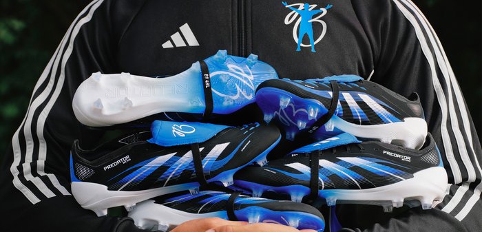 Des chaussures de football noires et bleues empilées, présentant un design élégant, un dessus texturé et une semelle bleue transparente avec des crampons ; étiquetées "Predator."