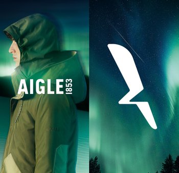 Veste imperméable verte avec un col haut et une grande capuche, arborant le nom de la marque "AIGLE 1853" en texte blanc. L'arrière-plan comprend des aurores boréales.