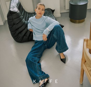 Hellblauer gestrickter Pullover mit gerippten Bündchen, übergroße dunkle Jeanshose, schwarze spitze Schuhe und ein texturierter schwarzer Sitzsack.