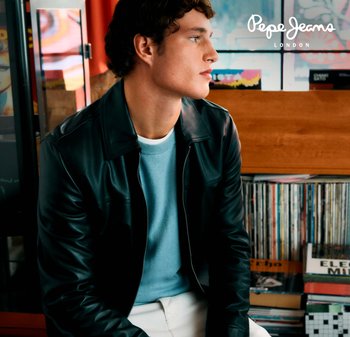 Chaqueta de cuero negra sobre un suéter azul claro, figura masculina sentada; pantalones blancos y fondo texturizado de discos de vinilo.