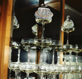 Kristallklockglas staplade med glittrande vätska, toppade med en färgglad paljettprydd myntbörs. En reflekterande spegelbakgrund förstärker djupet.