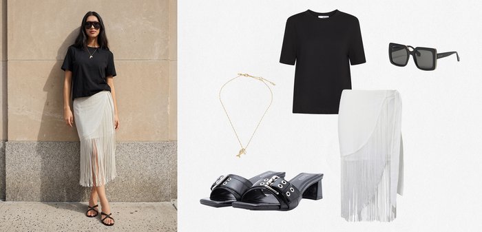 Femme portant un t-shirt noir, une jupe blanche à franges, des sandales noires, des lunettes de soleil et un collier doré ; des articles assortis sont exposés à côté d'elle.