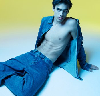 Jeansowa kurtka i luźne dżinsy w odcieniach niebieskiego, z nagim torsiem. Gładka tekstura, swobodny krój, na jaskrawożółtym tle.