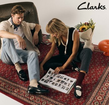 Black leather shoes with a glossy finish, casual attire, a patterned red rug, and a floral arrangement in a white vase are present.