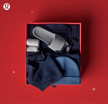 Sandali grigi, felpa blu navy a girocollo, berretto blu navy a coste, tre paia di calzini grigi in una scatola rossa su uno sfondo rosso.