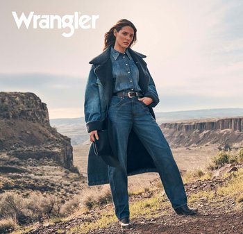 Denimjakke med saueskinnskrage, denimskjorte og vide jeans i mellomblå. Svart belte og cowboyboots, med en svart hatt i hånden.