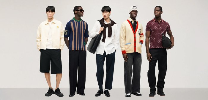 Fem män står på rad klädda i stilfulla, avslappnade kläder, inklusive shorts, byxor, cardigans, tröjor och accessoarer, mot en enfärgad bakgrund.