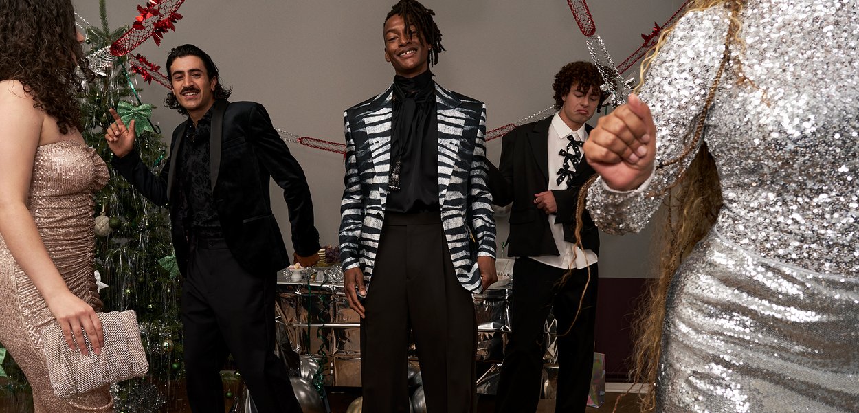 Neli inimese grupp tantsib piduliku ürituse ajal. Ühel on seljas hõbedaste litritega kleit, teisel must sametjakk ja kolmandal triibuline bleiser.