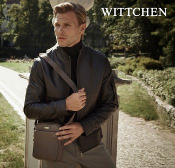 Brązowa skórzana kurtka o eleganckim kroju, noszona z czarnym golfem. Brązowa torebka na ramię ma srebrne elementy.