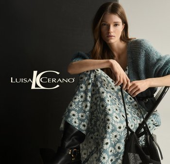 Woman sitting, wearing a light blue floral dress and a textured gray cardigan. Black knee-high boots and a black mesh handbag are visible.