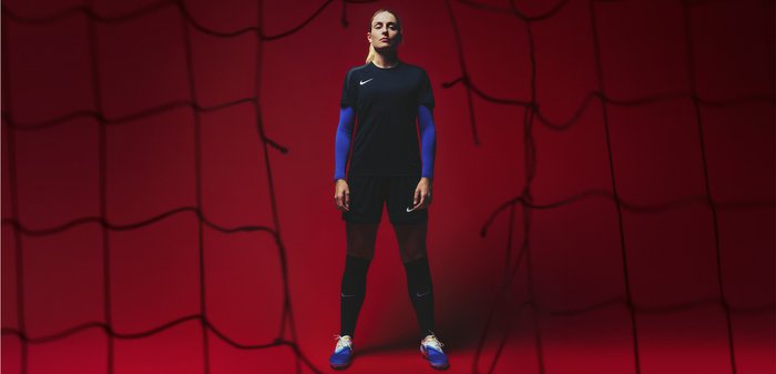 Maglia da calcio Nike con maniche corte nere, maniche lunghe blu, pantaloni corti neri e scarpini blu su uno sfondo rosso.