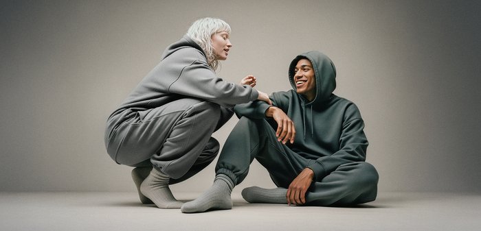 Grauer Hoodie und Jogginghosen-Set, getragen von zwei Personen. Der Stoff ist weich, mit lockerem Sitz und gerippten Bündchen, vor einem neutralen Hintergrund.