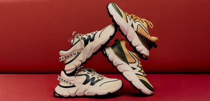 Divi pāri sporta apavu krēmkrāsā un zaļā tonī, sakārtoti un sabalansēti pret sarkanu fonu, ar biezām baltām zolēm un "WEEKEND" siksnām.