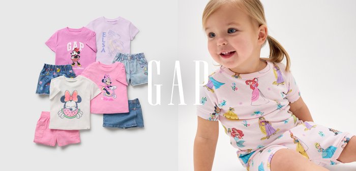 Et lille barn iført Disney-prinsesse-pyjamas ved siden af seks farverige babytøjsæt med Minnie og Disney-figurer med shorts og t-shirts.