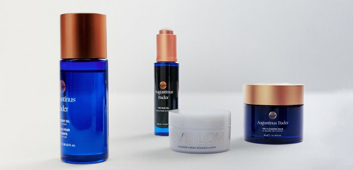 Quatre contenants cosmétiques : bouteilles et pots en verre bleu avec des couvercles en cuivre. Les produits incluent de l'huile pour le corps, de l'huile pour le visage et un baume nettoyant.