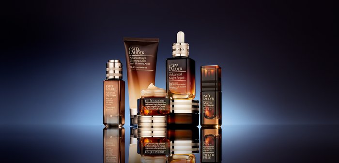 Cinq produits de soin Estee Lauder : flacons en verre foncé, de formes variées, avec des accents dorés et un emballage transparent ; étiquettes visibles avec les noms des produits.