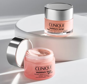 Two Clinique Moisture Surge jars: one with a silver lid and pink cream visible, and another with a clear lid, both labeled. Positioned on a white surface.