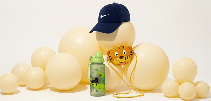 Bež baloni složeni s tamnoplavom Nike kapom, maskom s tigrastim licem i žutim trakama te zelenom bocom za vodu s dizajnom crne pantere.