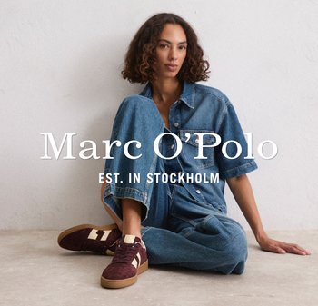 Denim overhemd en oversized jeans in blauw, gecombineerd met bordeaux sneakers met roomkleurige accenten. Neutrale achtergrond, model zit.