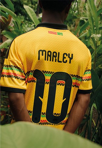 Person wearing a yellow shirt with "MARLEY" and the number "10" on the back, standing among green tropical plants.