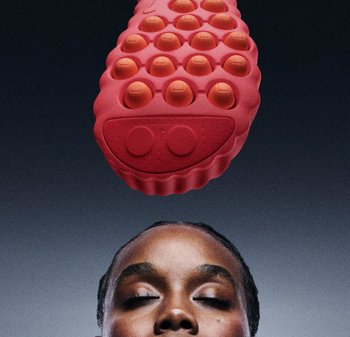 Masseur rouge texturé en forme d'ovale avec des nœuds circulaires surélevés sur le dessus. Positionné au-dessus de la tête d'une personne sur un fond sombre.