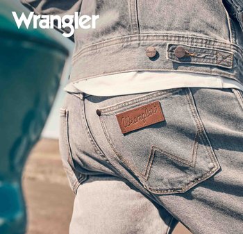 Ljust grå denimjeans har en brun läderlapp med "Wrangler"-logotyp och en klassisk broderad bakfickdesign. Jeansen bärs tillsammans med en vit skjorta.