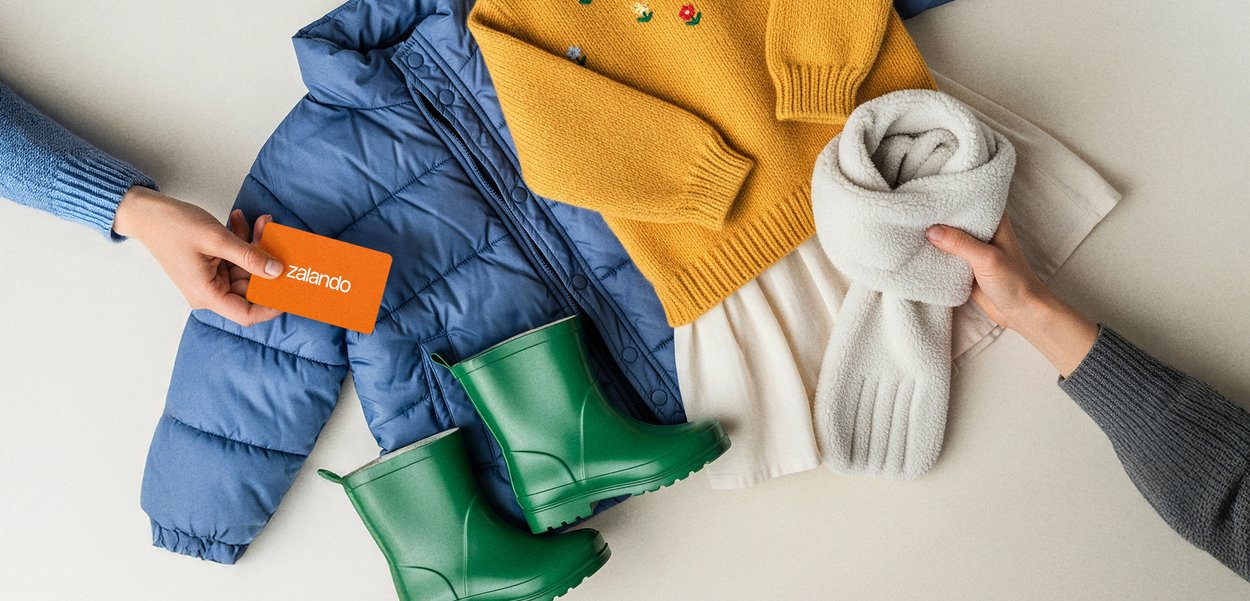 Chaqueta acolchada azul, suéter amarillo de punto con patrón floral, falda blanca, botas de goma verdes y bufanda de forro polar crema. Tarjeta de regalo naranja.