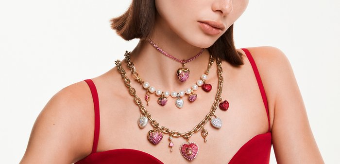 Vrouw met drie laagjes kettingen met gouden schakels, parels en hartvormige hangers versierd met roze en rode kristallen.